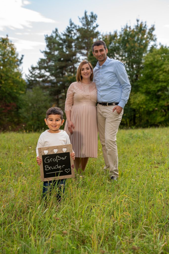 Eltern mit Sohn auf einer Wiese, der Junge hält eine Kreidetafel