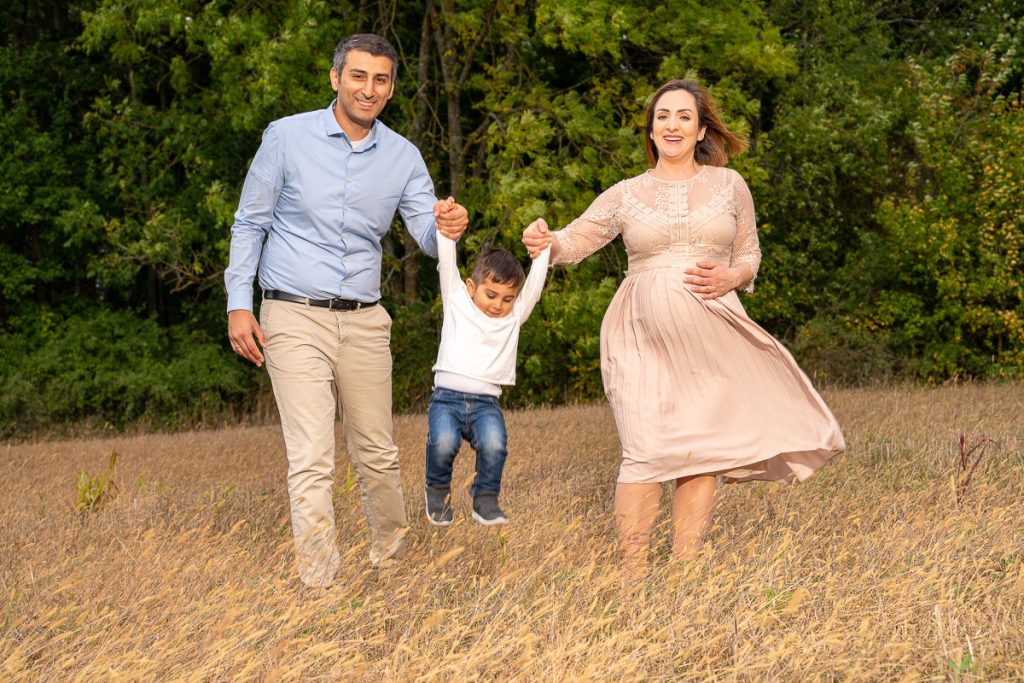 Eltern heben ihren kleinen Sohn an den Händen durch ein Feld, die Mutter ist schwanger