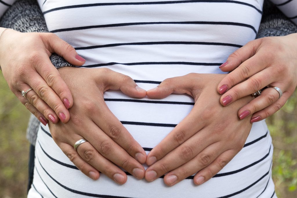 Hände formen ein Herz auf dem Babybauch