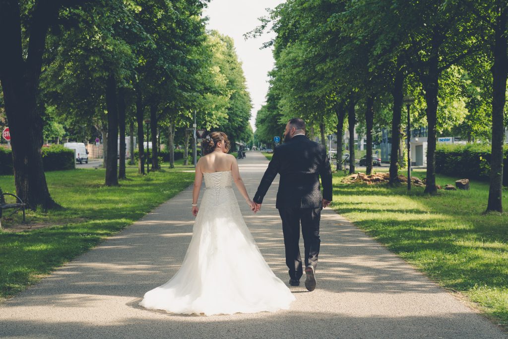 Brautpaar von hinten auf einem Weg durch eine Allee